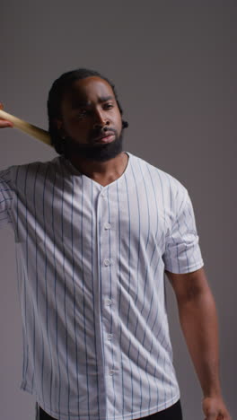 Vertical-Video-Studio-Portrait-Of-Serious-Male-Baseball-Player-Wearing-Team-Shirt-Holding-Bat-And-Throwing-Ball-In-The-Air-Shot-Against-Grey-Background-2