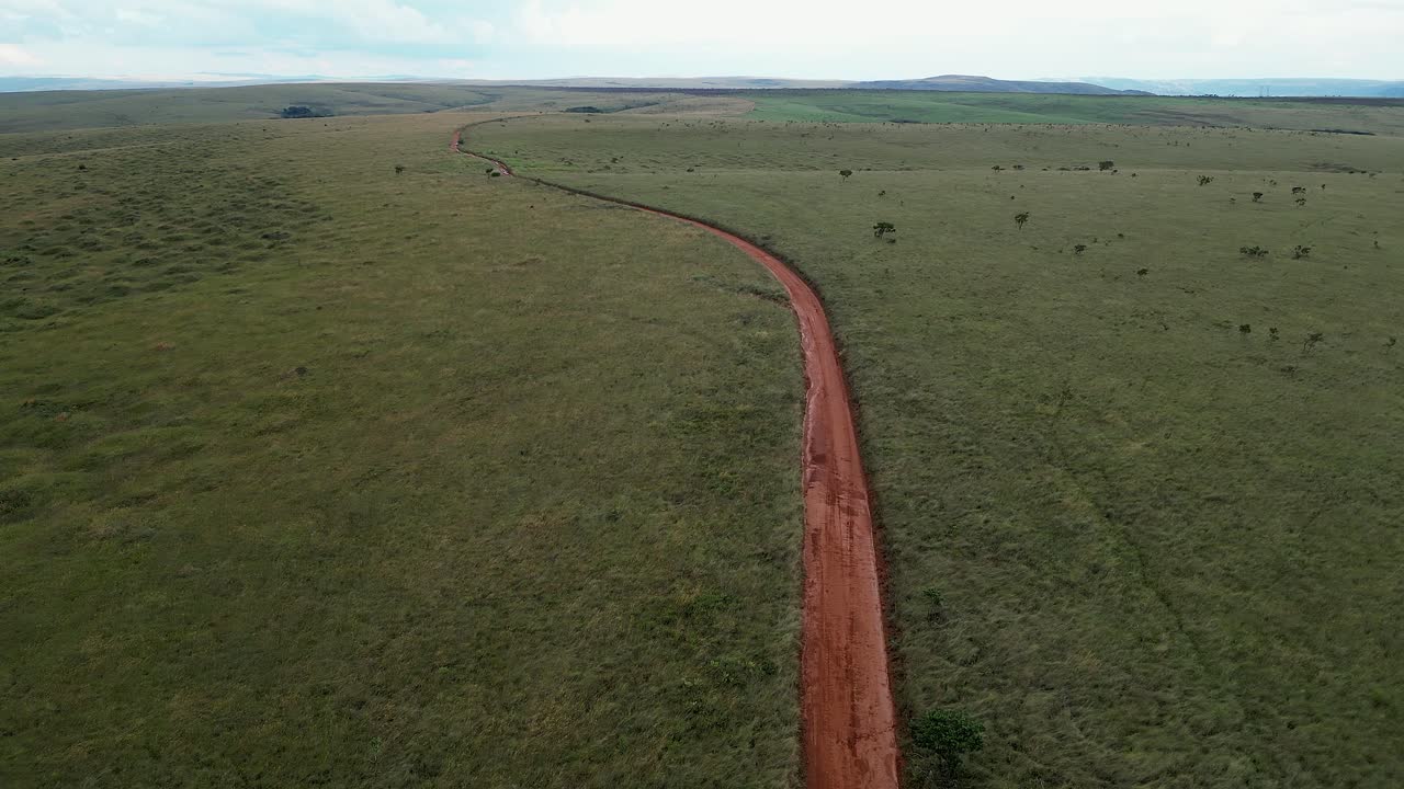 Low aerial follows red dirt road through expansive green Pantanal