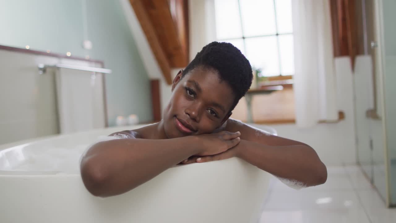 Portrait of african american attractive woman relaxing in foam bath and smiling in bathroom