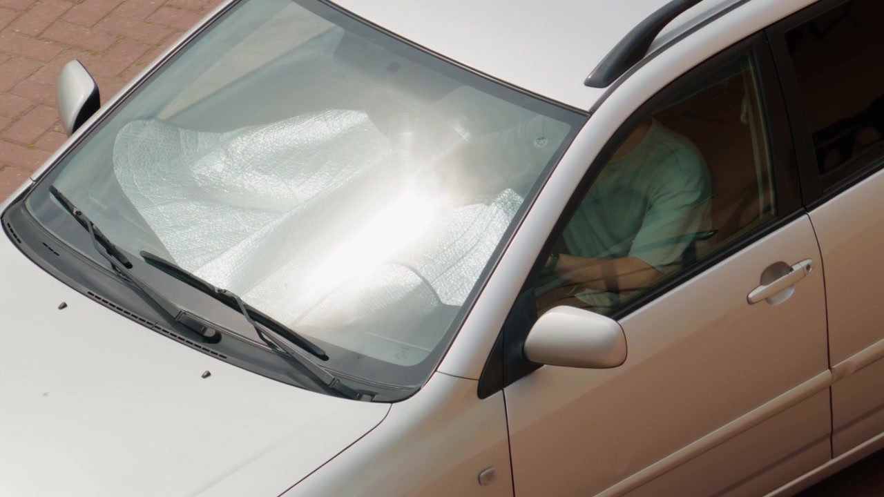 Vista dall'alto di un'auto bianca in movimento con parasole riflettente sul parabrezza che protegge l'interno dal calore estivo durante una giornata di sole