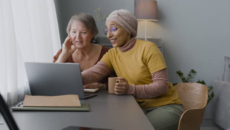 arabic woman teaching an elderly woman to use a laptop at home 1