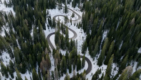 Vista-Aérea-Del-Camino-Sinuoso-A-Través-Del-Paso-Giau-Cubierto-De-Nieve-Rodeado-De-Bosque-Alpino