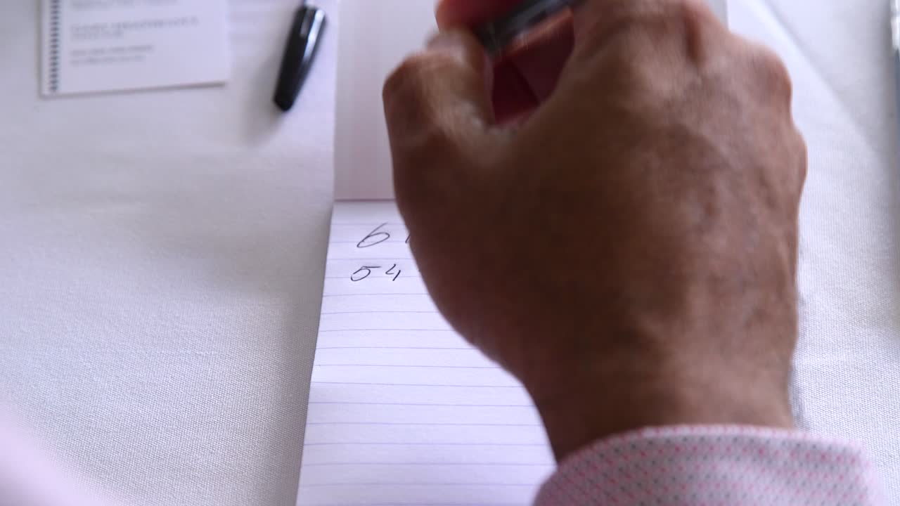 Close up of male hands writing on a pad of white paper with a pen