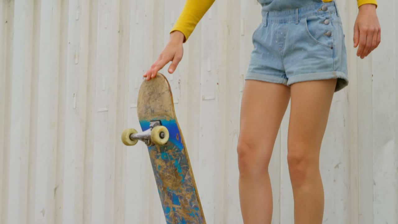 Vista frontale di giovane donna caucasica con lo skateboard in piedi sulla rampa in uno skatepark 4k