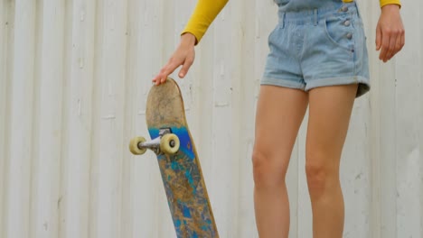 Front-view-of-young-caucasian-woman-with-skateboard-standing-on-ramp-at-skateboard-court-4k