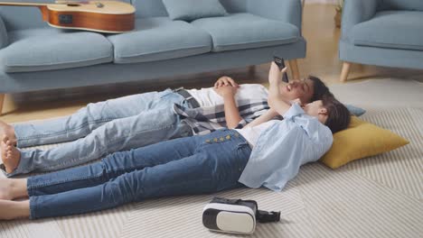 asian teen couple recording voice message on smartphone while lying on carpet on the floor at home