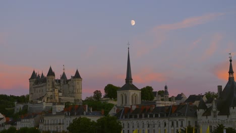 panning up shot of moon rising directly above church spire with beautiful multicolored sunset sky with château in french town of saumur during summer months 4k