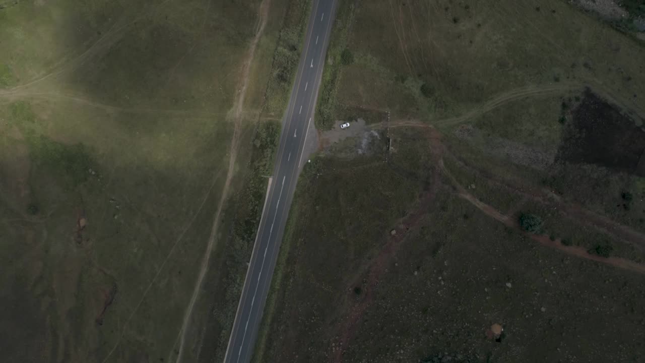 A white car is stopped by the side of the road, with nothing around it but grass and walking paths.