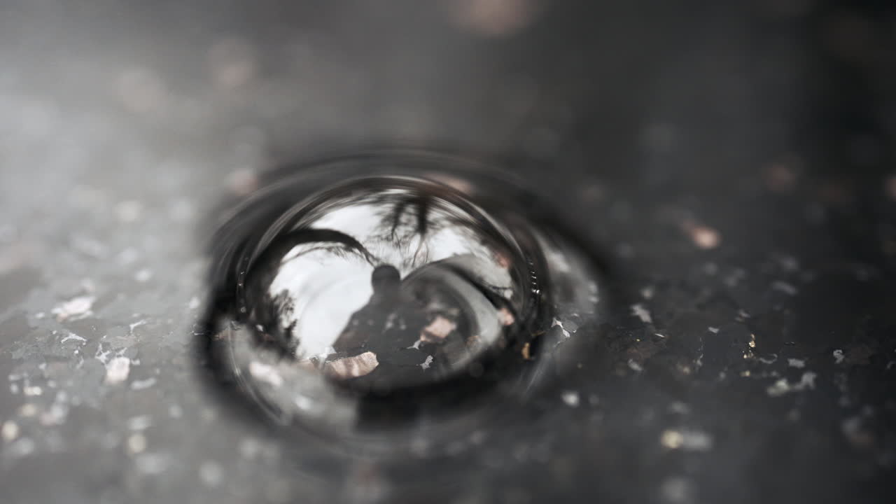 Close up shot of water droplet forming ripple on wet reflective surface