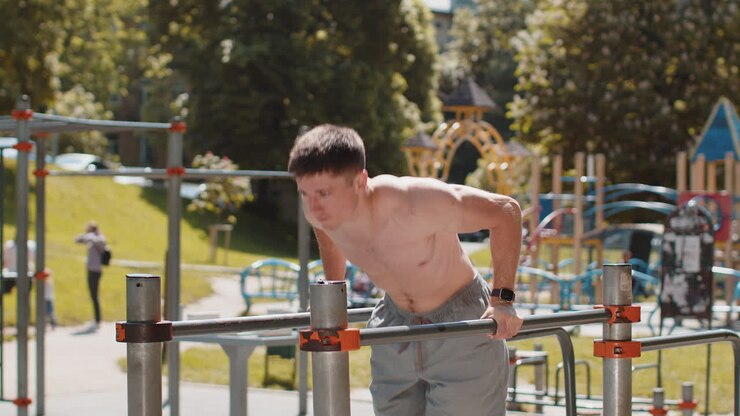 Athletic caucasian muscular man practicing dips on parallel bars training triceps on playground