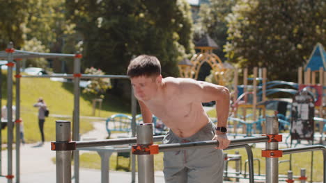Athletic caucasian muscular man practicing dips on parallel bars training triceps on playground