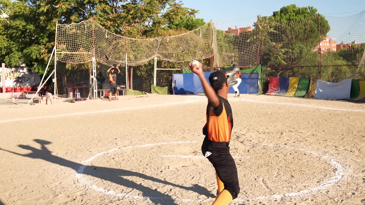 Arremessador de beisebol lançando uma bola em um campo de terra.