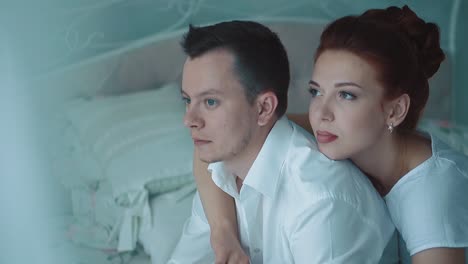 Young-beautiful-couple-sitting-in-the-morning-on-the-bed-they-are-looking-out-the-window-thoughtfully