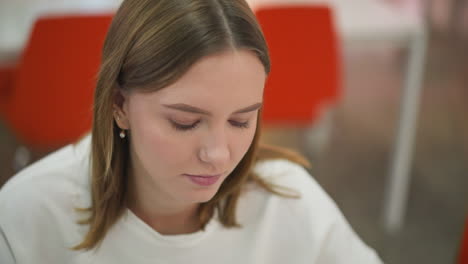 primer plano de una mujer joven mirando hacia abajo en concentración pensativa, ambientado en un ambiente interior moderno con acentos naranjas vibrantes en el fondo
