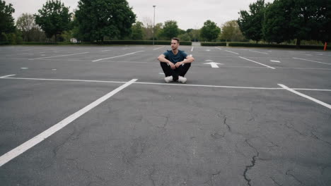 man crouching alone in an empty parking lot