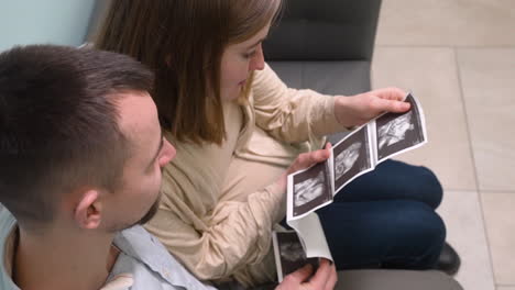 vista superior de la mujer embarazada y su esposo viendo imágenes de ultrasonido en la consulta médica