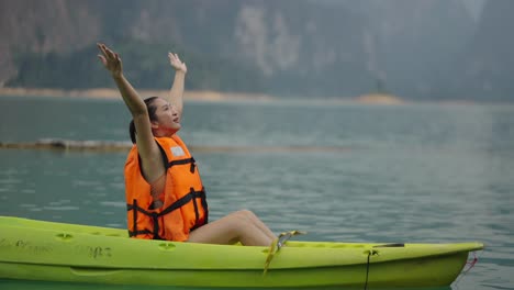 woman enjoying kayaking on a serene lake with arms raised in joy