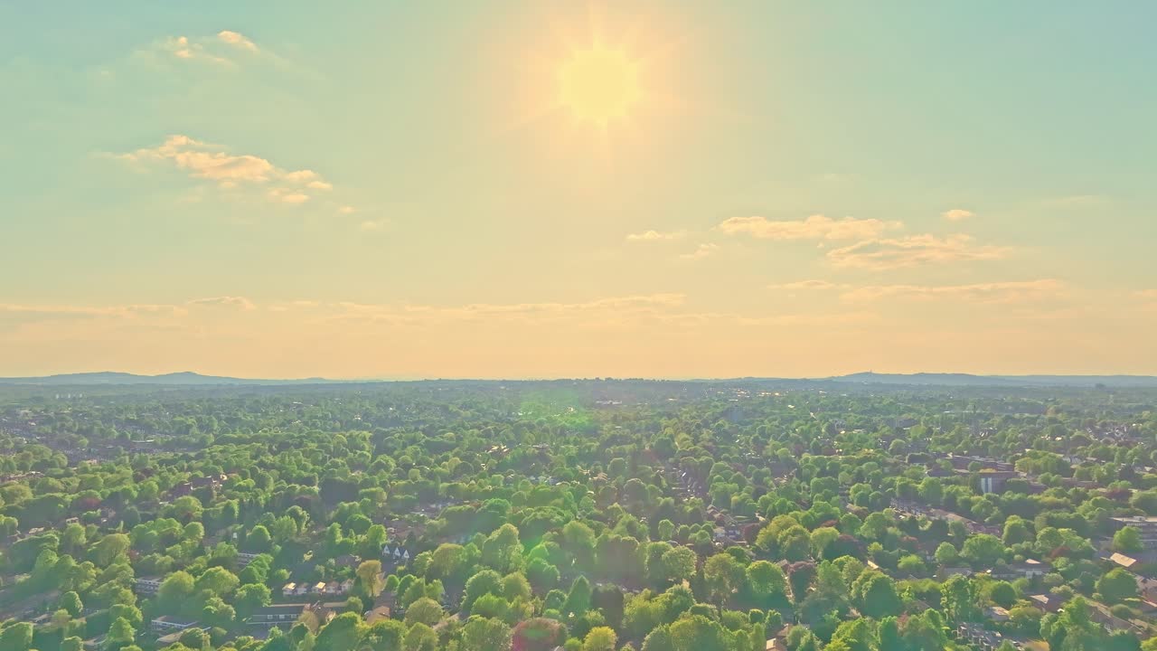 Panoramic view of Birmingham Botanical Gardens during sunset with sun shining through clouds and green trees covering residential houses, creating a peaceful and scenic landscape