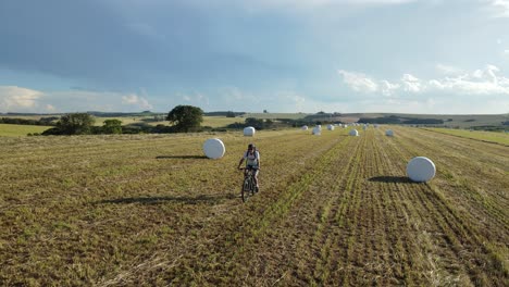 cyclist passing between silage of rolled hay wrapped in a harvested field, drone view