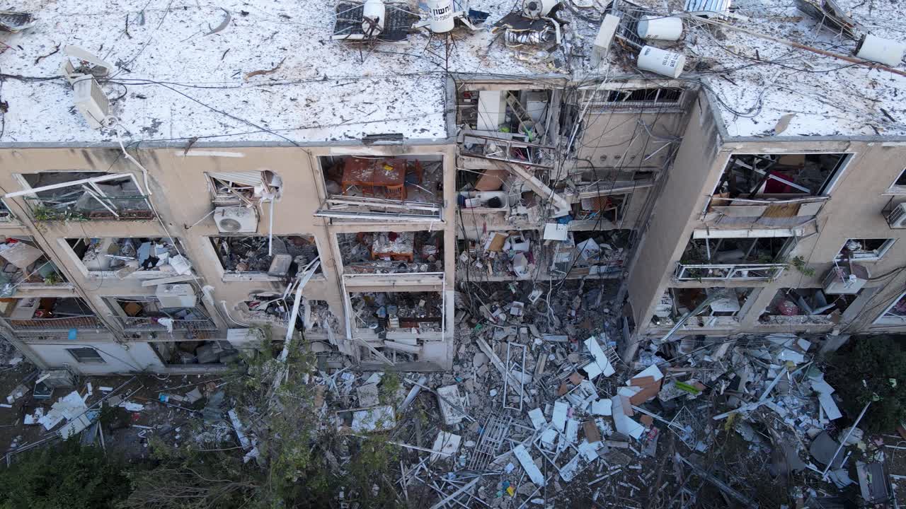 Drone glides sideways in top-down view over damaged building and exposed interiors in Tel Aviv