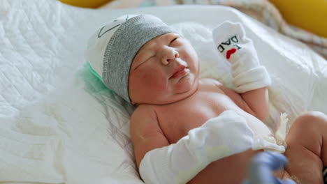 sweet new born baby in a cap and mittens. nurse's gloved hands changing a diaper to a caucasian infant. close up.