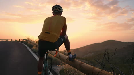 A-mobile-phone-captures-the-moment-as-a-helmeted-professional-cyclist,-equipped-for-sports,-stands-at-the-mountain's-edge,-taking-in-the-scenic-view-in-slow-motion