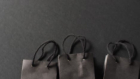 three black gift bags with black handles in a row on dark grey background with copy space