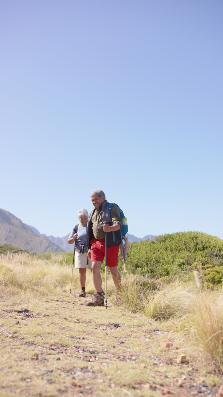 Vertical video of senior biracial couple hiking in mountains, in slow motion