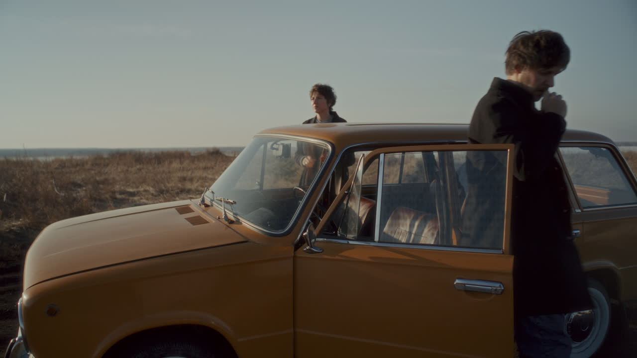 Couple Smoking by Vintage Car during Stop on Road Trip in Open Field