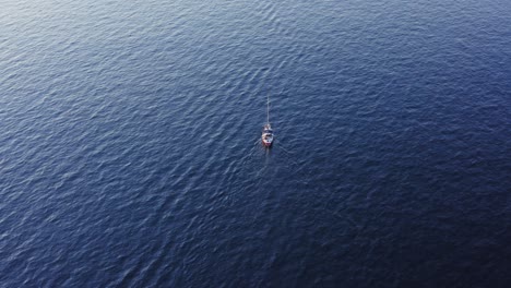 sailboat travelling through blue ocean waters, rising aerial tilt view