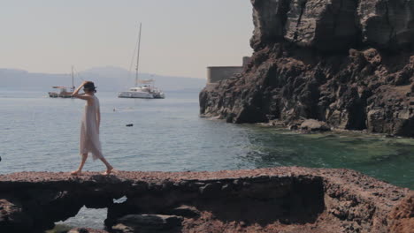 una mujer camina a lo largo de una playa rocosa viendo los pequeños barcos y catamarán