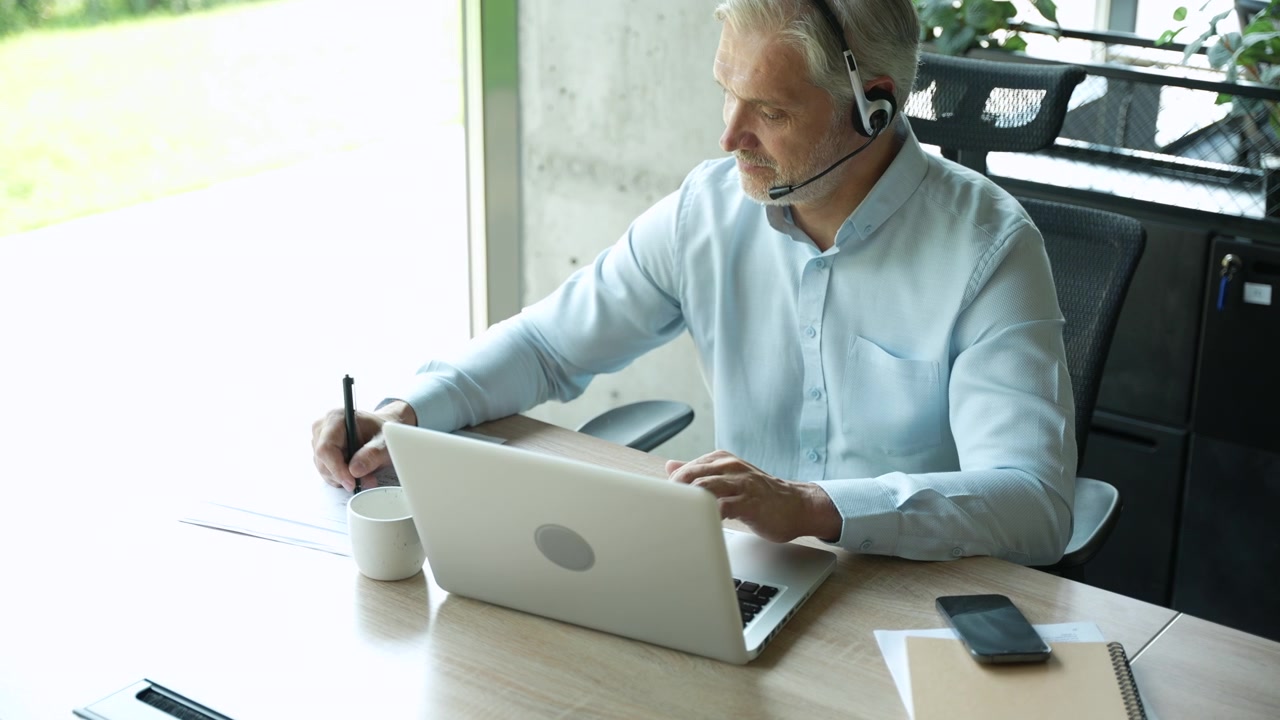 Ervaren zakenman werkt op laptop en maakt aantekeningen in een modern kantoor.