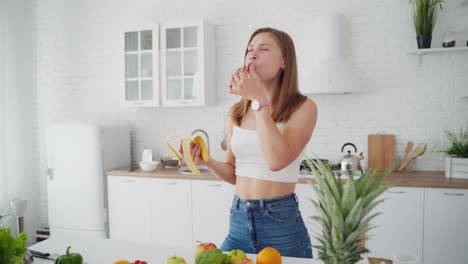 slim woman with banana in the kitchen. beautiful girl in the modern light kitchen. young female eats sweet banana and throws banana peel on the floor.