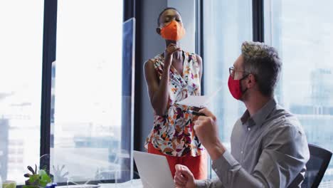 Diverse-male-and-female-office-colleagues-discussing-while-writing-on-glass-board-at-modern-office