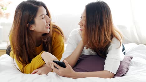 젊은 아시아 레즈비언 커플이 집의 침실에서 스마트폰에 앱을 사용하고 있습니다.