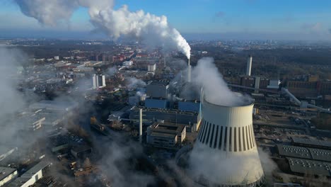 Aerial view of a thermal power plant emitting smoke on a sunny day, with a river and a city in the background. Lovely aerial view flight drone shot footage from above
