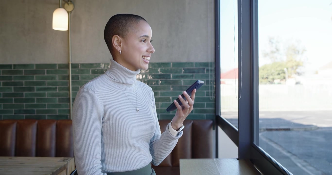 Donna afroamericana alla finestra di un caffè che controlla lo smartphone, scorre, parla, risponde a un messaggio