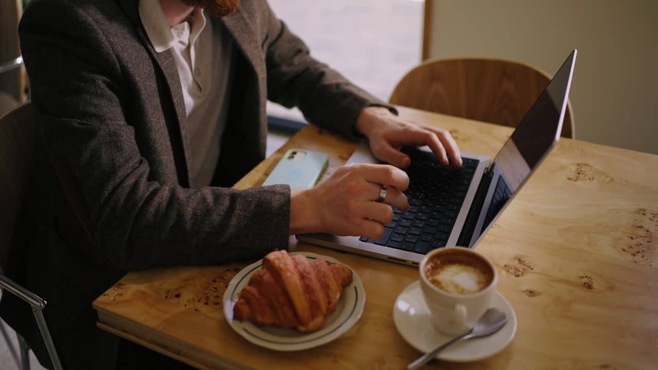 hombre trabajando en su computadora portátil en un café con un croissant y café
