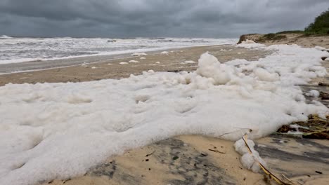 una escena de playa tormentosa con espuma marina lavándose en la orilla, bajo cielos nublados, capturando las secuelas de un ciclón