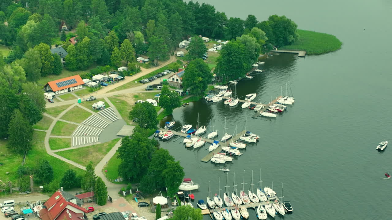 Lakeside town with boats in the marina, surrounded by green fields and forest, aerial view