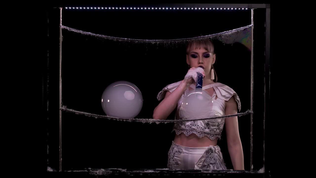 Stylish girl does tricks with soap bubbles. She blows two large bubbles with pipe