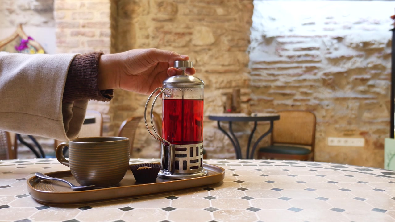 Close-up of Hand Pressing Red Tea in French Press at Cafe