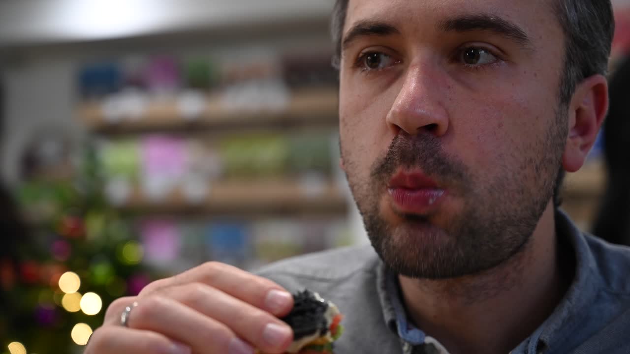 Close up of a man eating a burger with black buns