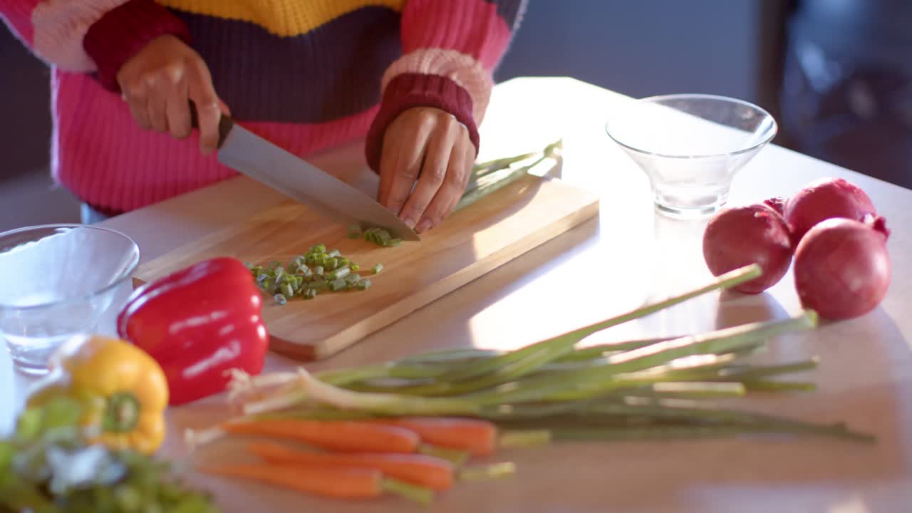 sección media de una mujer afroamericana cortando verduras en una cocina soleada