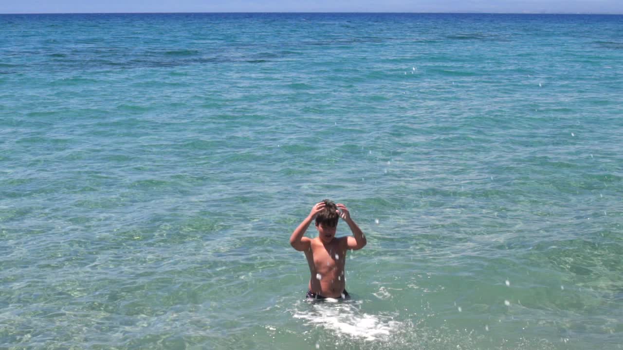 Ragazzo greco caucasico che gioca nelle acque cristalline del mare di Kalamata, Grecia, Peloponneso.