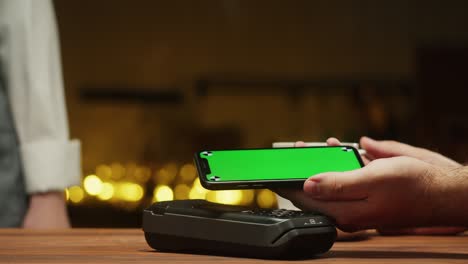 pagar por teléfono inteligente con pantalla verde cromada de primer plano. comprar sin dinero en efectivo en un restaurante o cafetería. comprar café utilizando el concepto de pago sin contacto y sin contacto. tecnología nfc y terminal bancario.