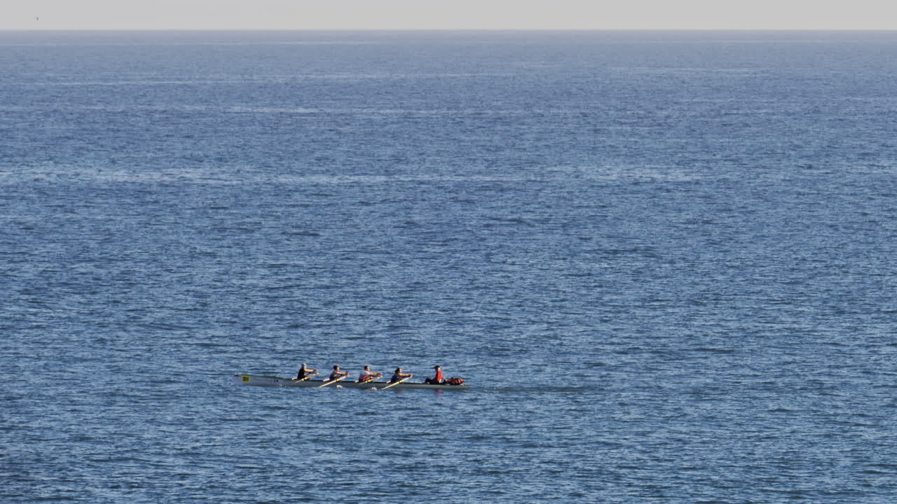 Distant view of a rowing team of four people practicing on calm water, with a coxswain seated at the front