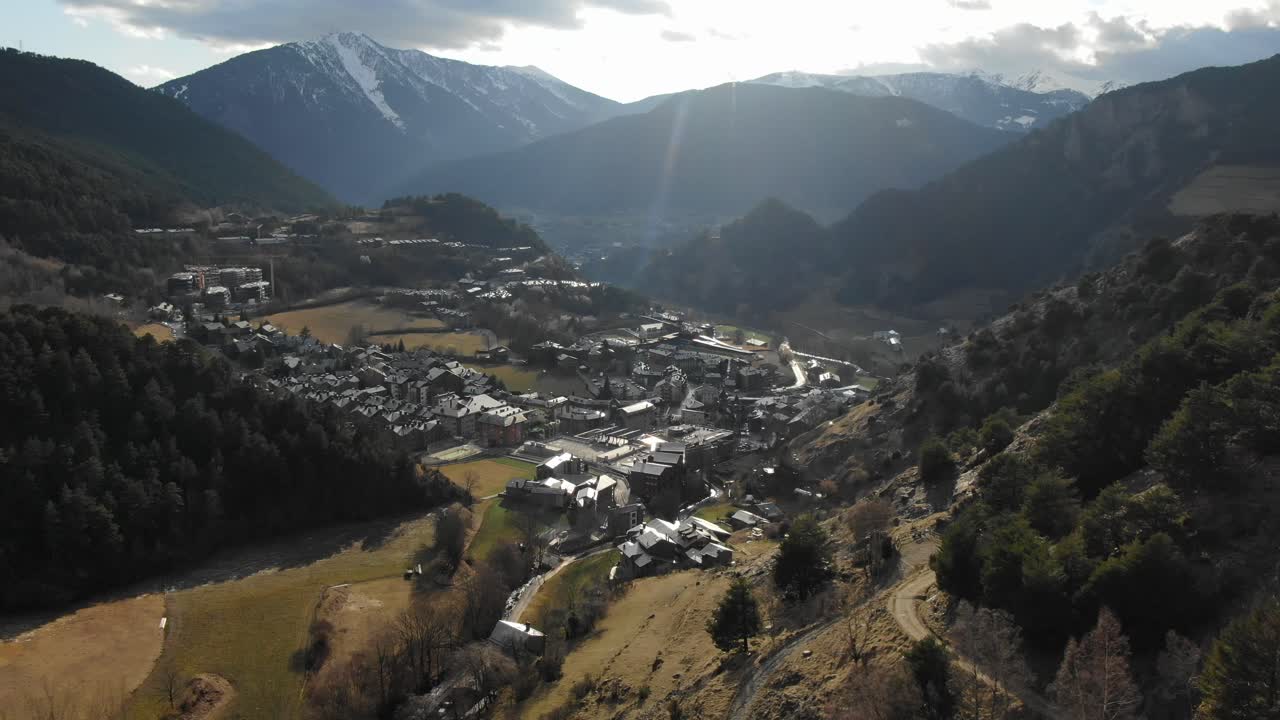 Aerial view of mountain village in Andorran valley with sun flare over peaks. Scenic alpine town, Pyrenees travel destination, establishing shot
