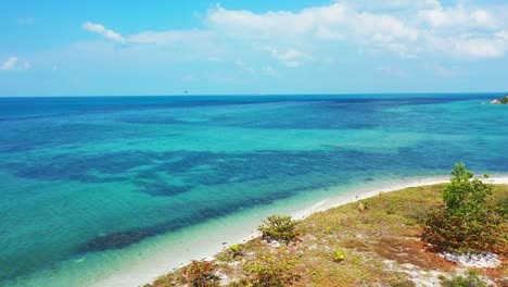 Bermuda-coast,-small-sandy-beach,-turquoise-sea-water-and-bright-blue-sky-with-fluffy-clouds