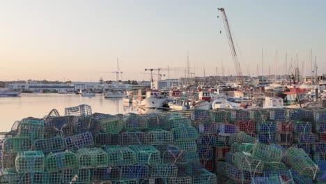 stacks of colorful fishing traps laying on the shore of lagos harbor with fishing boats and crane in the background